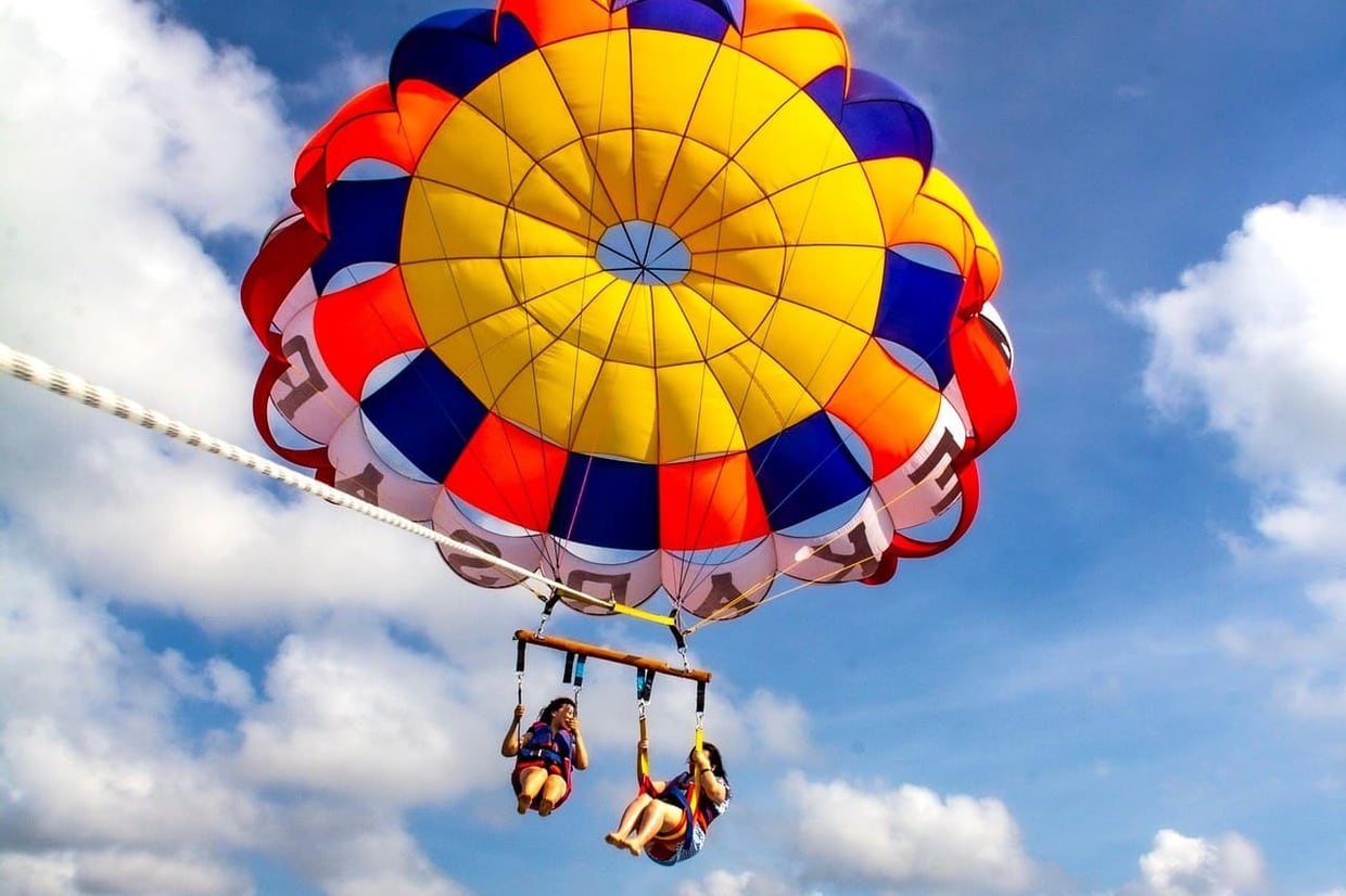 Colorful parasailing canopy above Budva with two passengers suspended over blue sky
